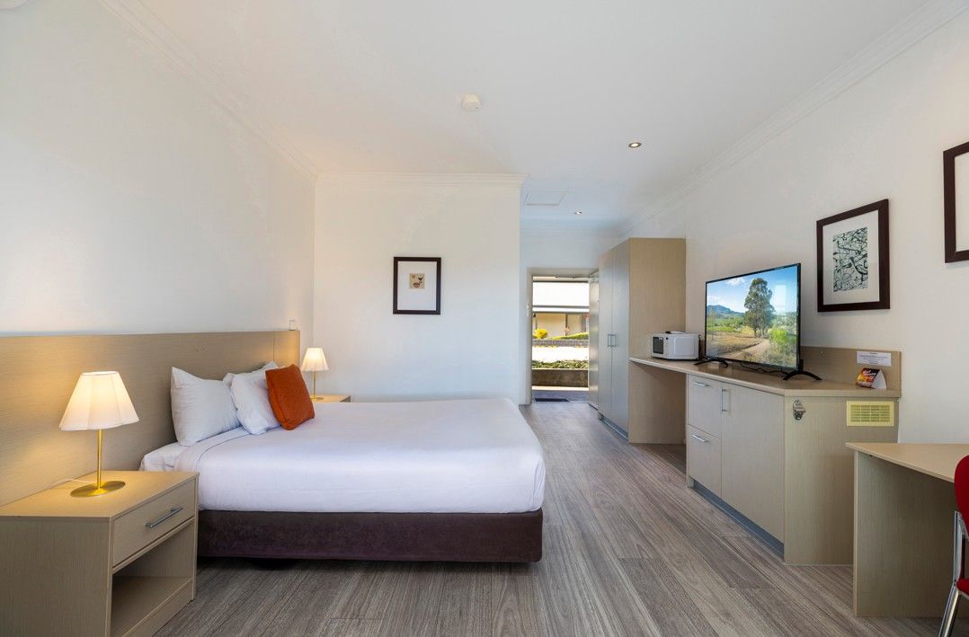 A hotel room with a bed, bedside tables, a desk, a television, and framed pictures on the wall.