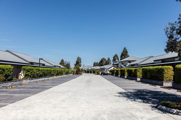 A long, straight pathway leading to a row of modern buildings with grey roofs, surrounded by neatly trimmed hedges and trees. - Hunter Gateway Motel (Rutherford)