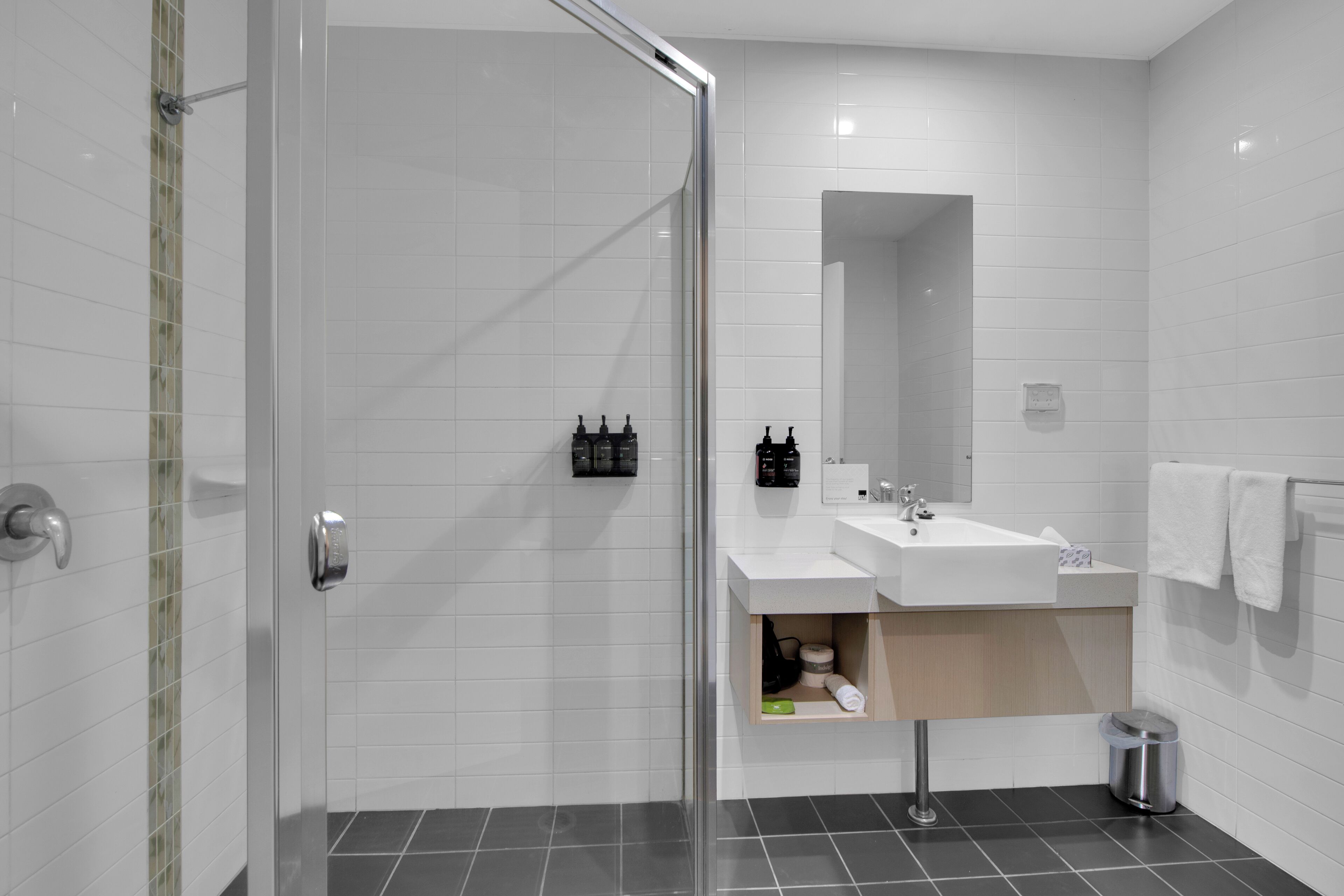 Ein modernes Badezimmer mit Duschabtrennung aus Glas, einem weißen Waschbecken und einem Spiegel.
