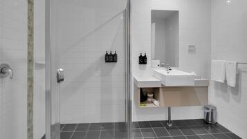 Ein modernes Badezimmer mit Duschabtrennung aus Glas, einem weißen Waschbecken und einem Spiegel.