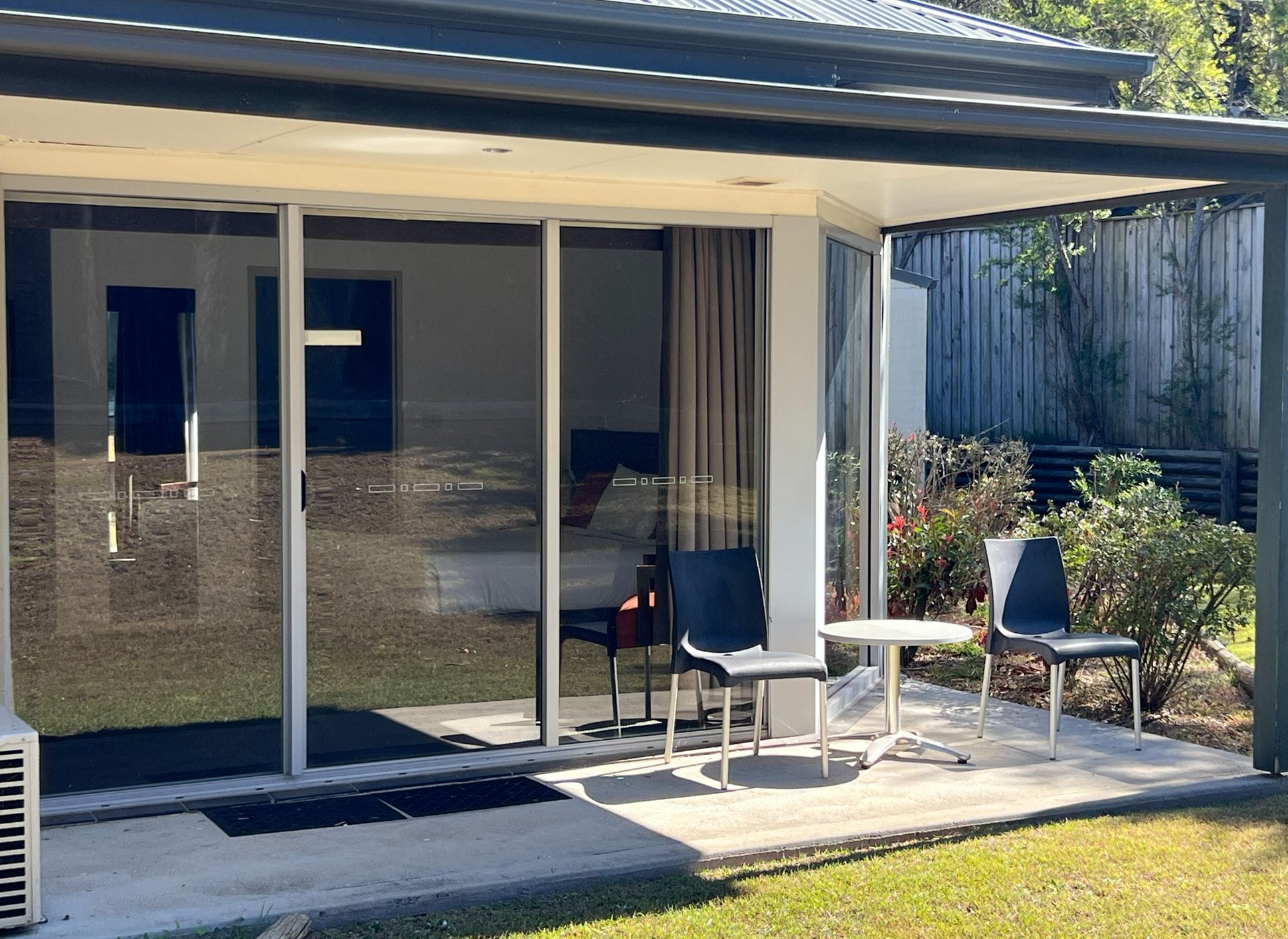 Une terrasse extérieure moderne, dotée d’une véranda en verre, de deux chaises et d’une petite table.