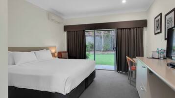 Hotelkamer met een bed, een bureau, een stoel, een televisie en een schuifdeur naar een achtertuin.
