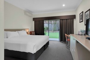 Habitación de hotel con cama, escritorio, silla, televisor y puerta corrediza de vidrio que da a un patio.