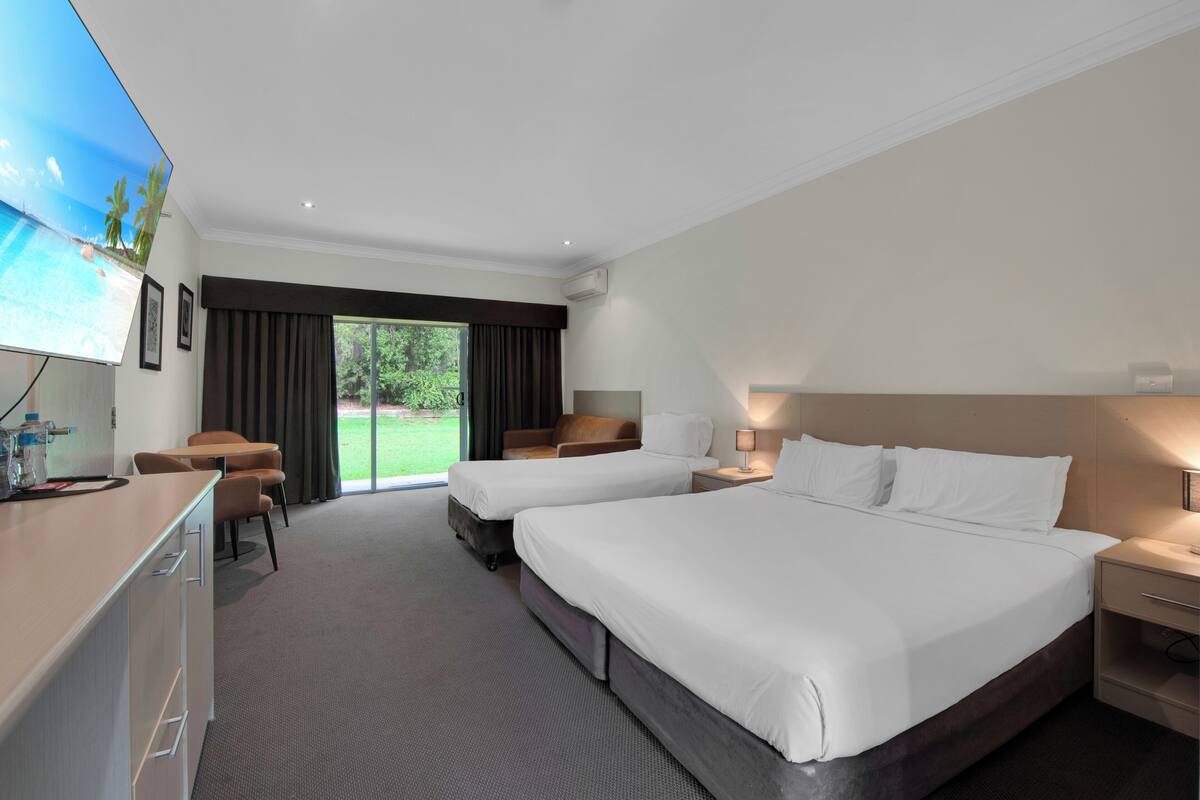 A hotel room with two beds, a desk, a chair, and a TV.