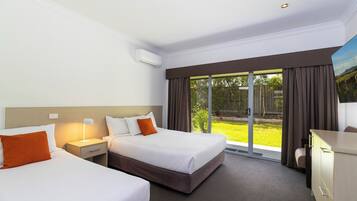 Habitación de hotel con dos camas, un escritorio, una silla y un ventanal con vistas a un jardín.