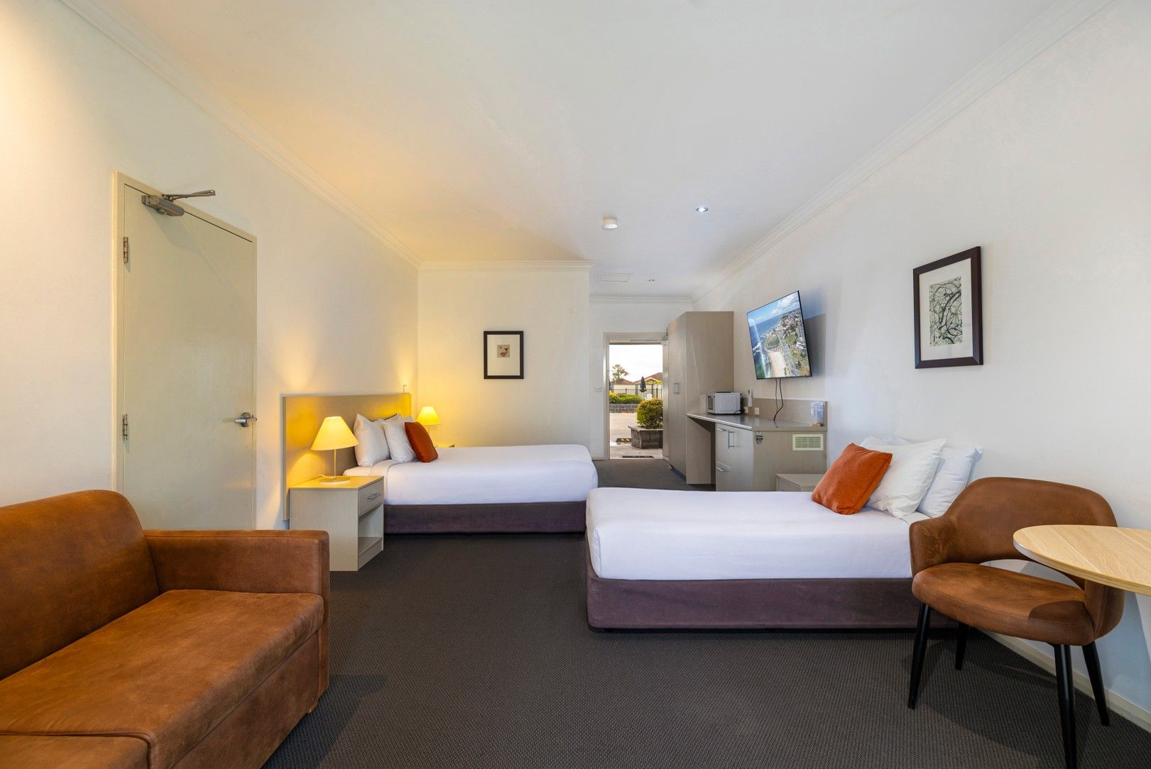 A hotel room with two beds, a desk, a TV, and a seating area.