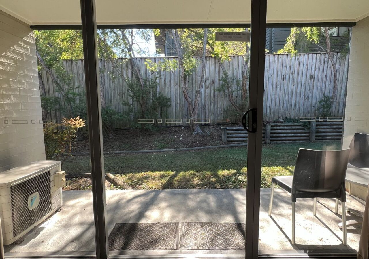 A patio area with a sliding glass door, a concrete floor, and a wooden fence in the background.