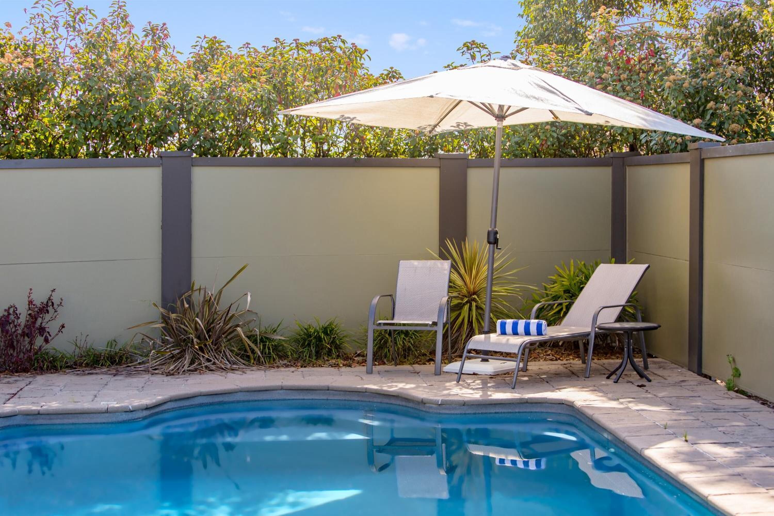 A swimming pool with two lounge chairs and a sun umbrella.