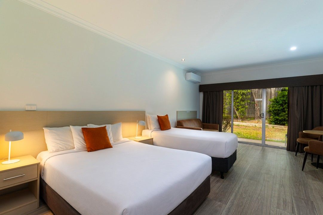 A hotel room with two beds, a desk, and a view of the outdoors.
