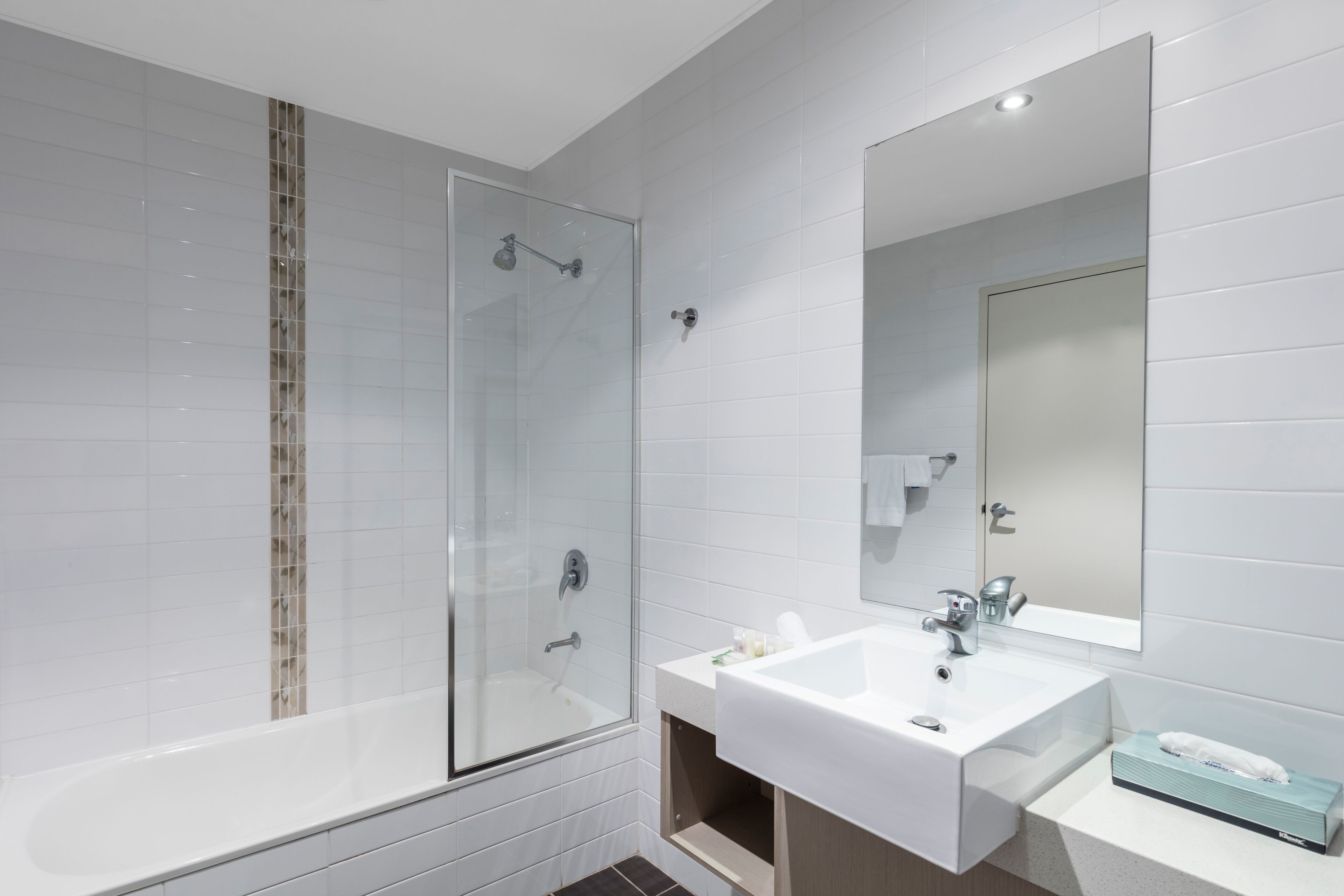 Un baño moderno con ducha envuelta en vidrio, un lavamanos blanco y un espejo encima.