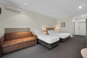 A hotel room with two single beds, a brown sofa, a small table, and a door leading to a bathroom. - Hunter Gateway Motel (Rutherford)