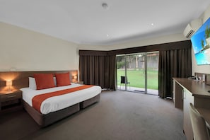 A hotel room with a large bed, a desk, a chair, a TV, and a sliding glass door to a garden. - Hunter Gateway Motel (Rutherford)