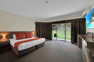 Una habitación de hotel con una cama grande, un escritorio, una silla, un televisor y una puerta corrediza de vidrio a un jardín.
