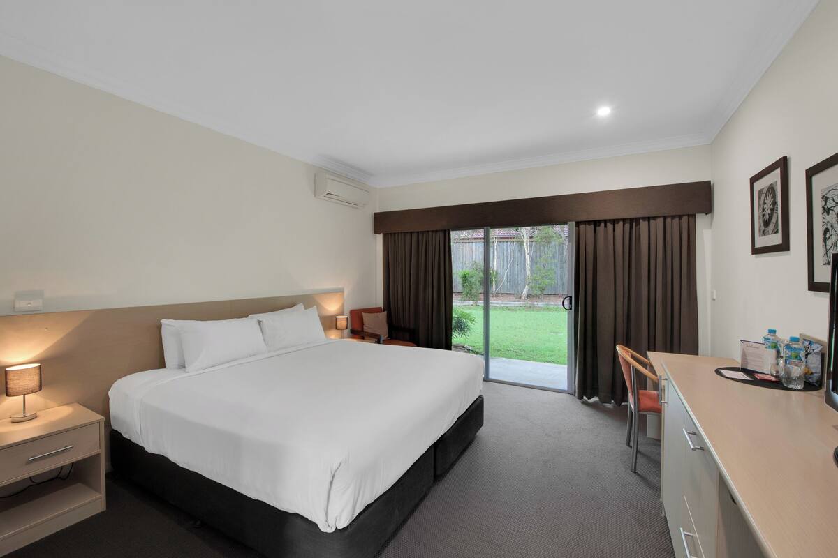 A hotel room with a large bed, a desk, a chair, and a view of the outdoors.
