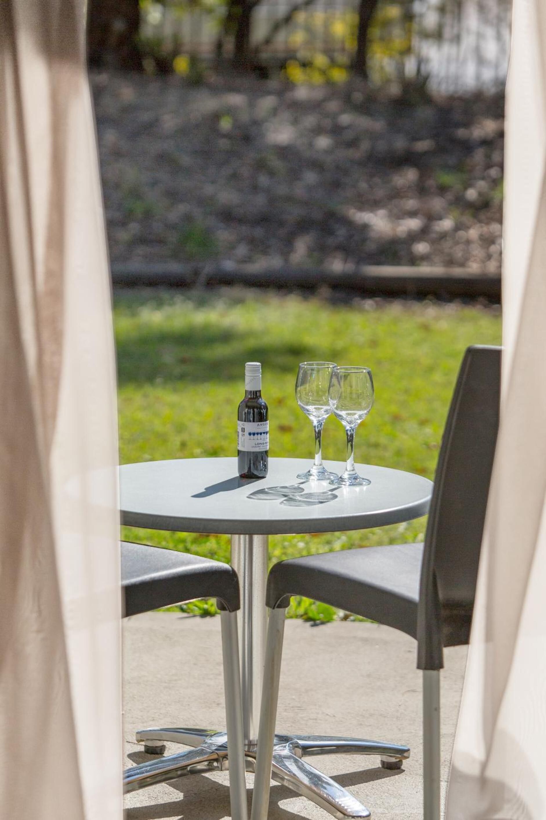 Een ronde tafel met een fles en twee glazen, buiten gezet met stoelen.