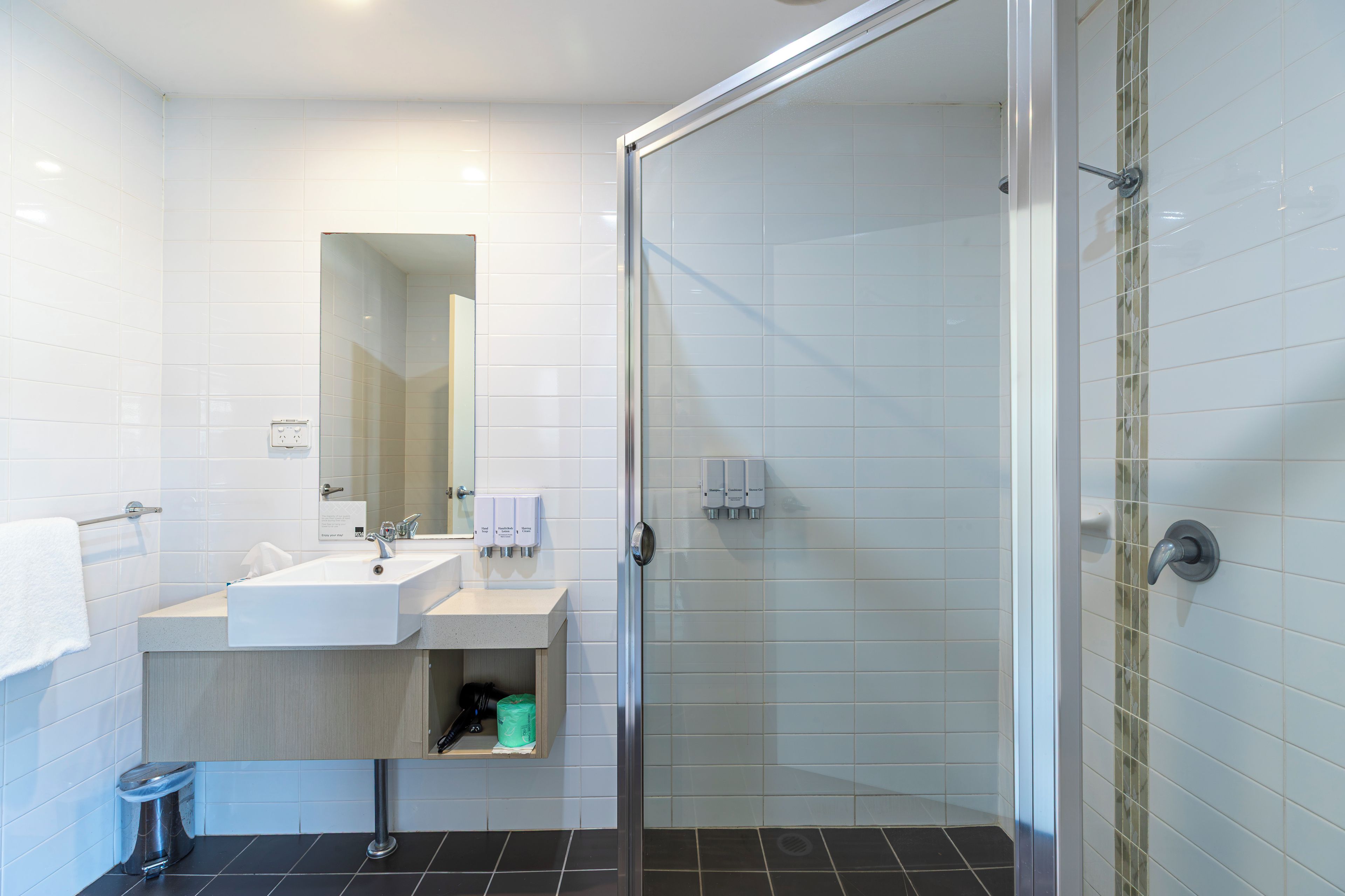 A modern bathroom with a glass shower enclosure, a sink with a mirror, and a towel rack.