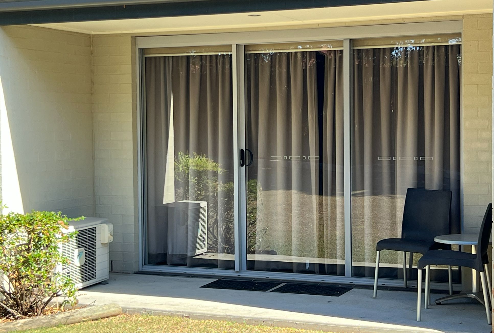 Un espacio exterior techado con puerta corrediza de vidrio, una mesa pequeña y una silla.