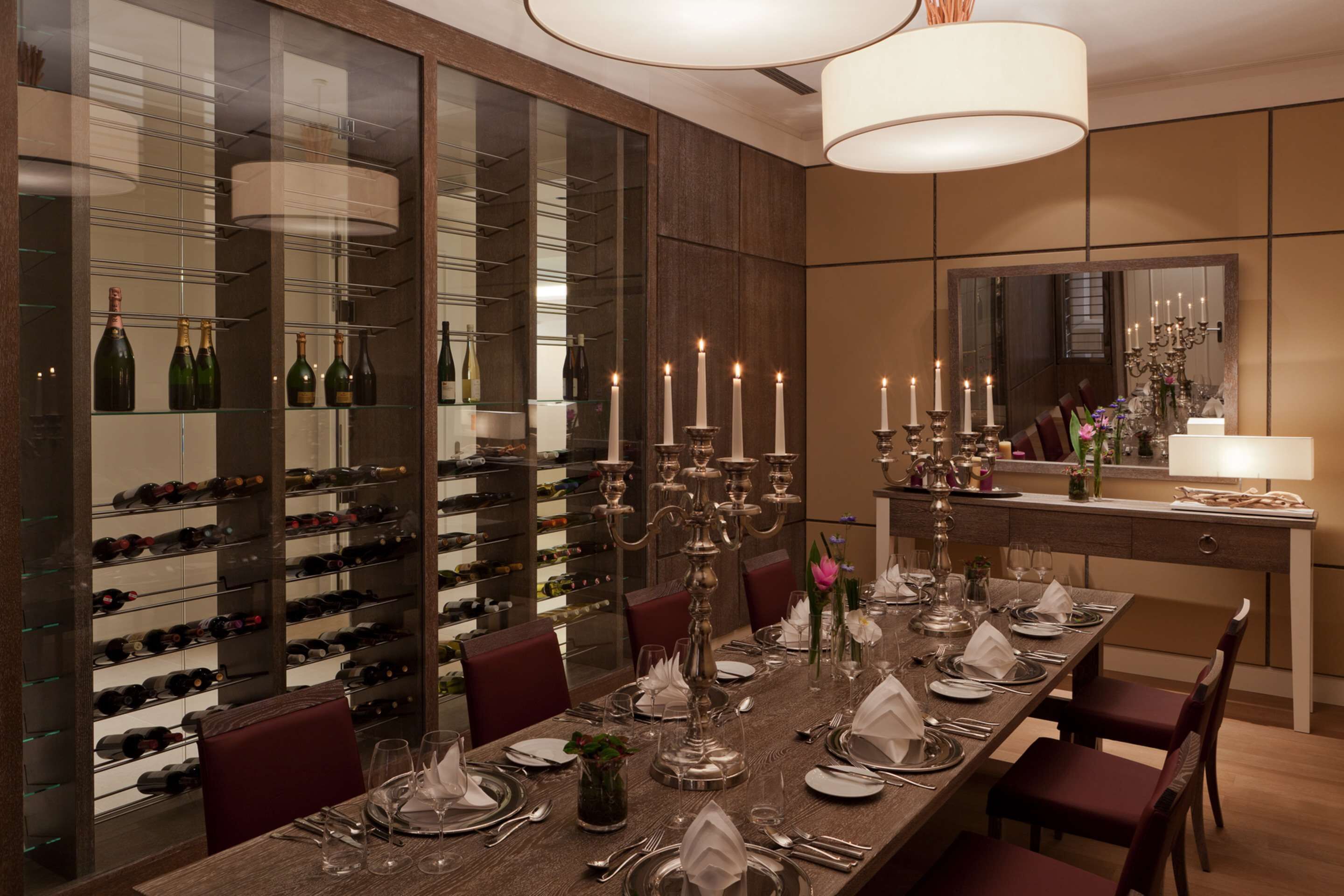 A dining area with a long table set for a meal, surrounded by wine racks and a mirror.