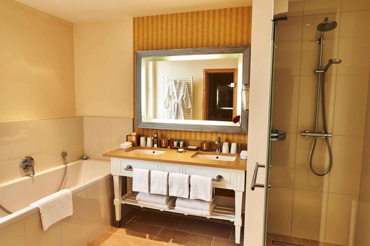 A bathroom with a bathtub, two sinks, a large mirror, and a shower area.