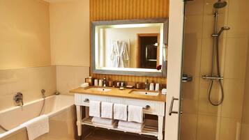 A bathroom with a bathtub, two sinks, a large mirror, and a shower area.