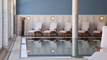 A pool area with six lounge chairs aligned along the poolside, a decorative column, and a tiled floor.