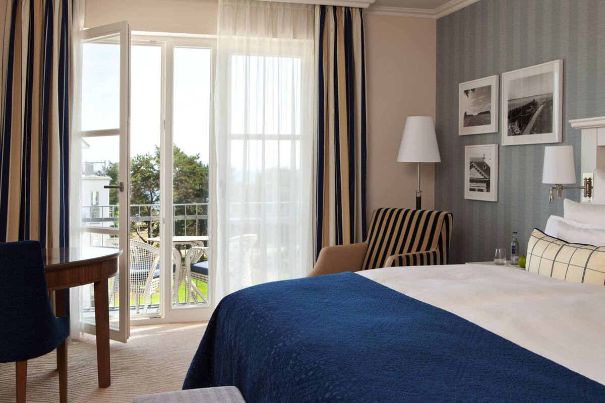 A hotel room with a bed, a desk, a chair, and a balcony with outdoor furniture.