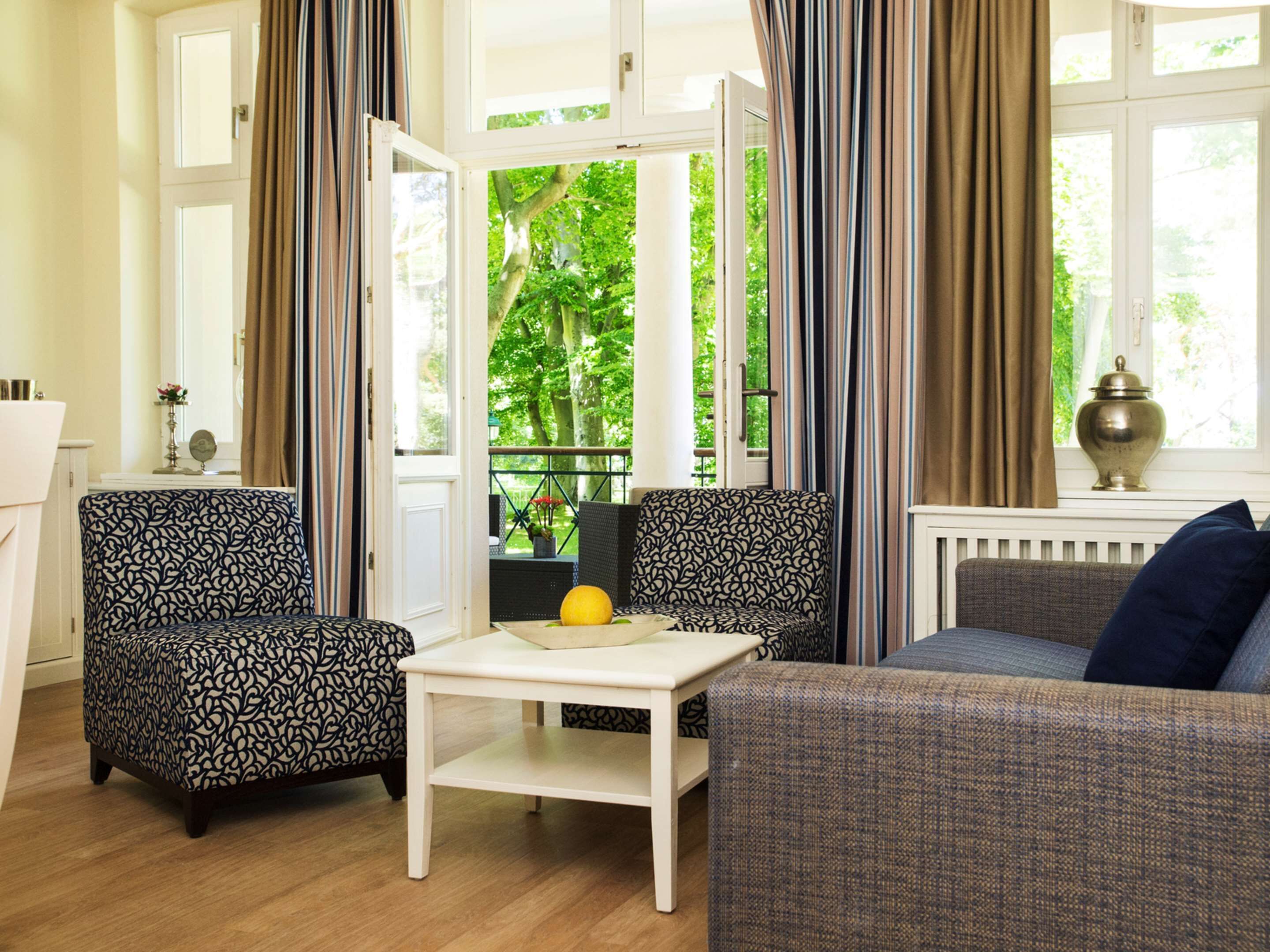 A living room with patterned sofas, a white coffee table, and a view of greenery through large windows.