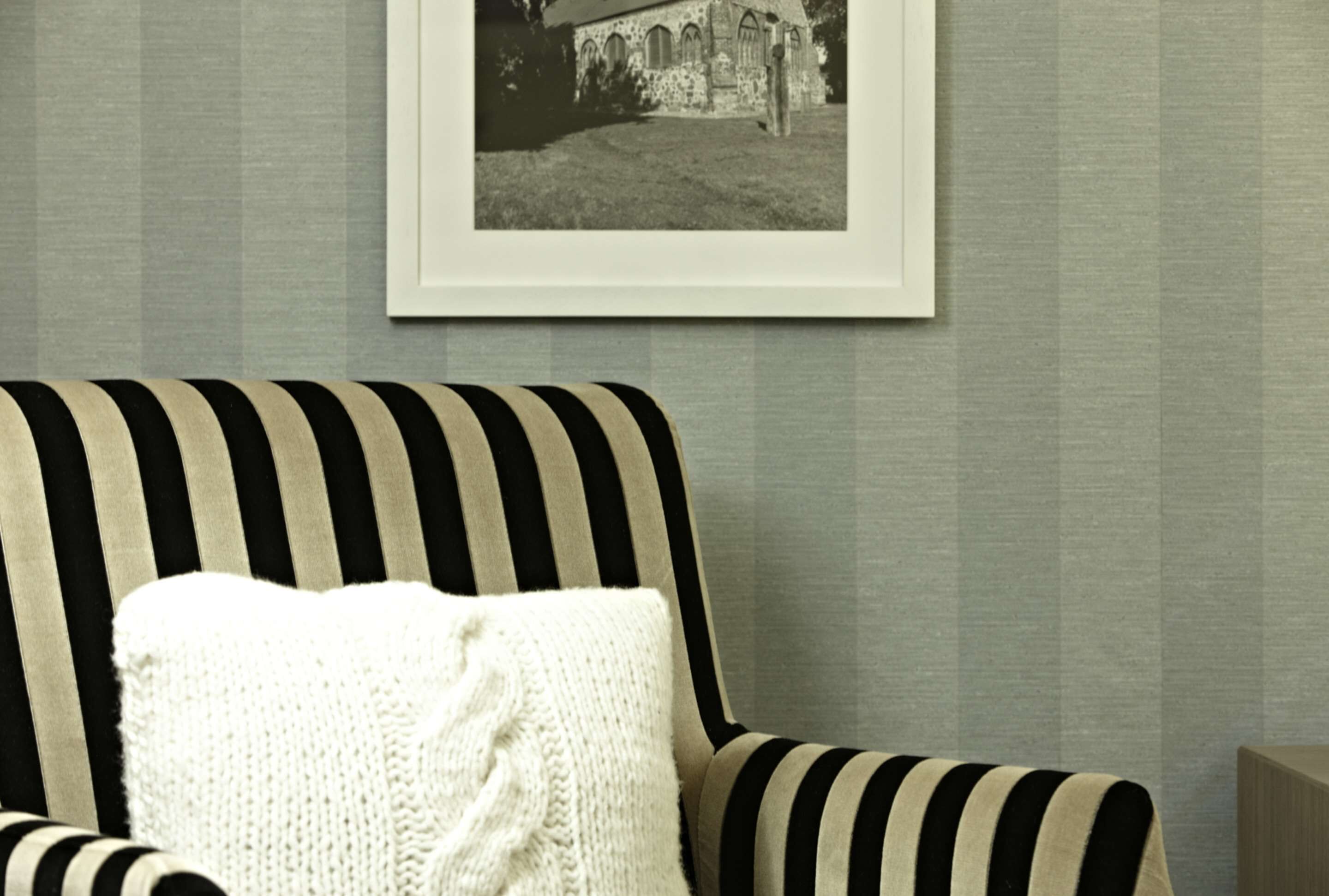 A striped armchair with a white knitted throw, positioned against a textured wall with a framed black and white photograph above it.