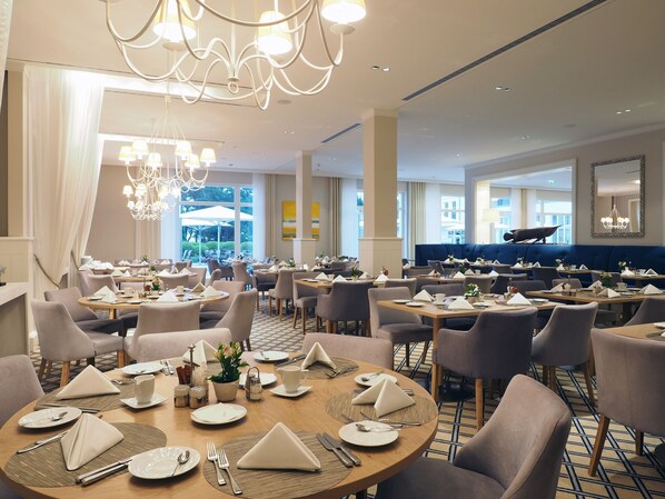 A well-lit dining area with round tables, chairs, and a blue booth seating area. - Steigenberger Grandhotel & Spa (Heringsdorf)