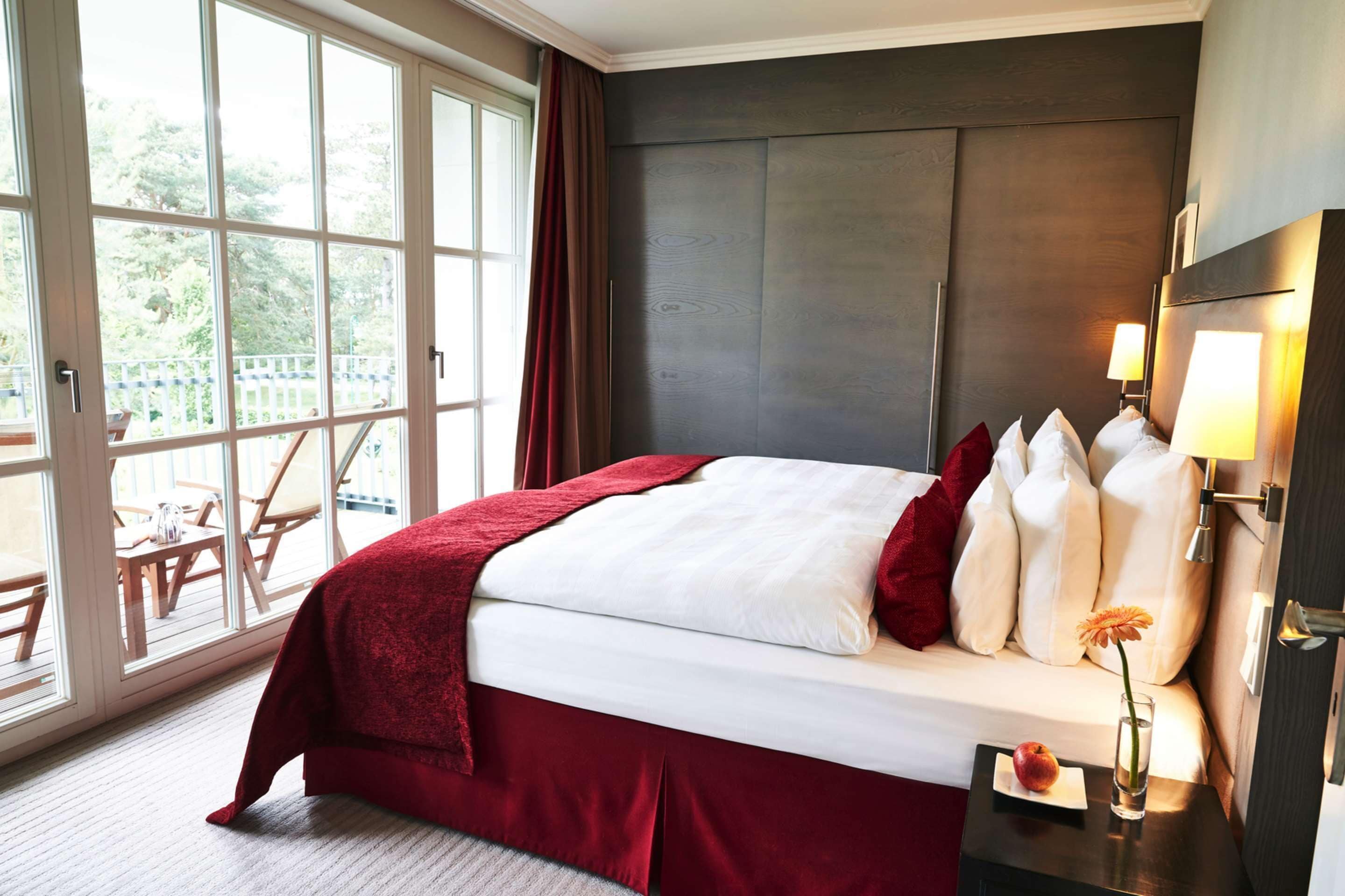A hotel room with a large bed, a nightstand with a lamp, and a view of an outdoor deck.