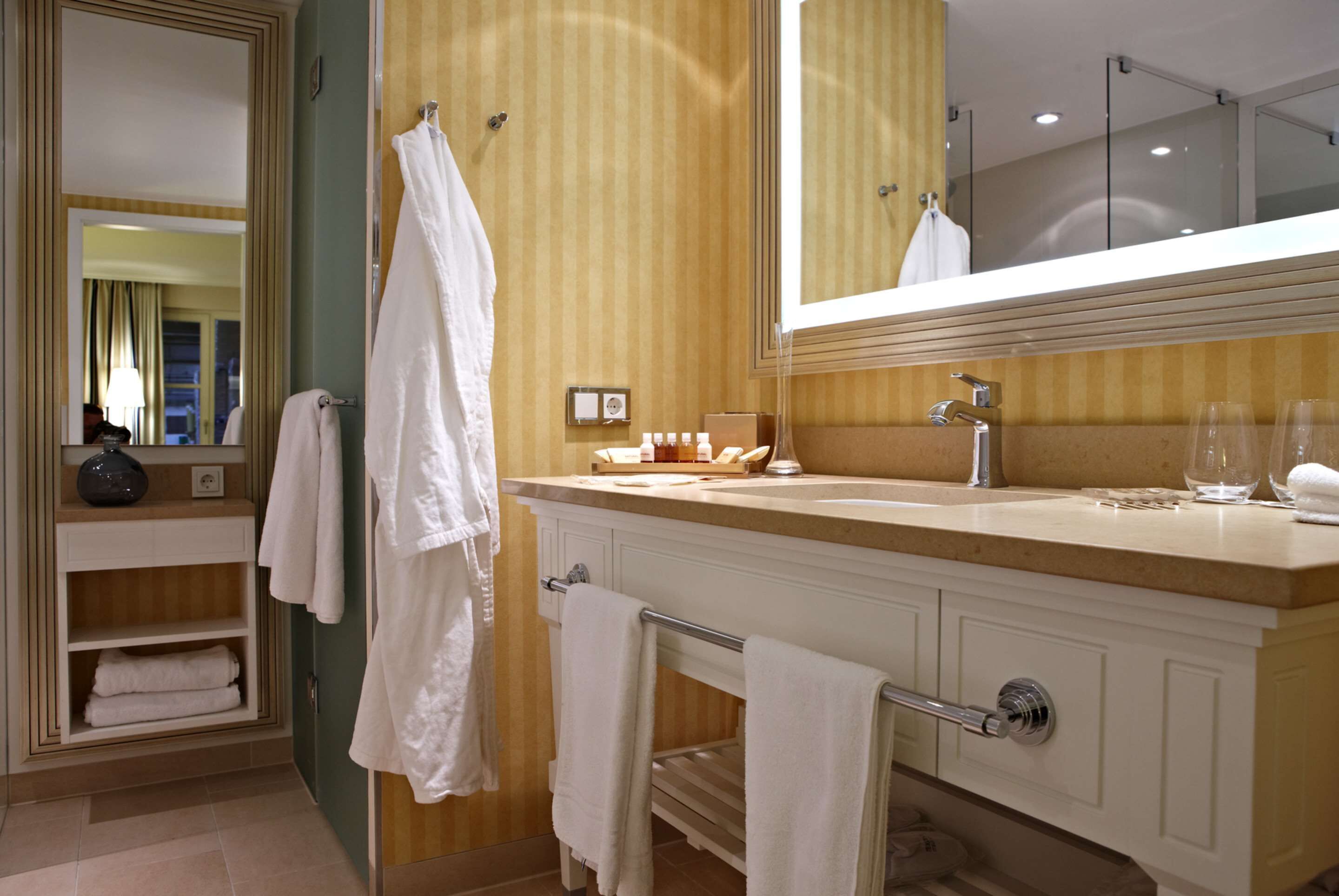 Un baño con un espejo grande, un lavamanos con toallero y un mueble de tocador con espejo.