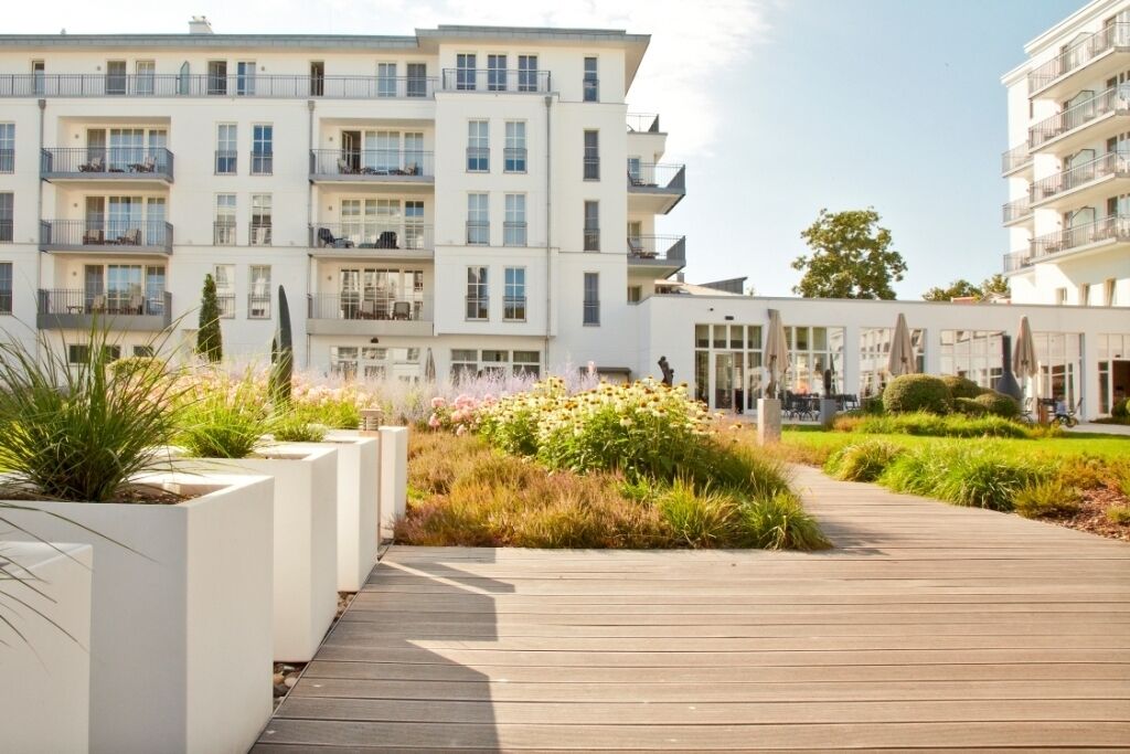 A modern apartment building with balconies, a wooden boardwalk, and landscaped gardens.