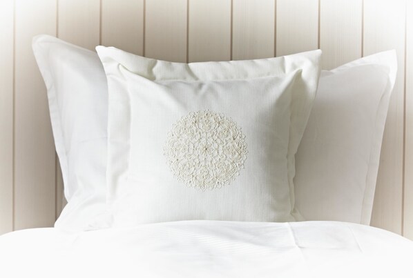 A white pillow with a circular embroidered design on a bed against a wooden headboard. - Steigenberger Grandhotel & Spa (Heringsdorf)