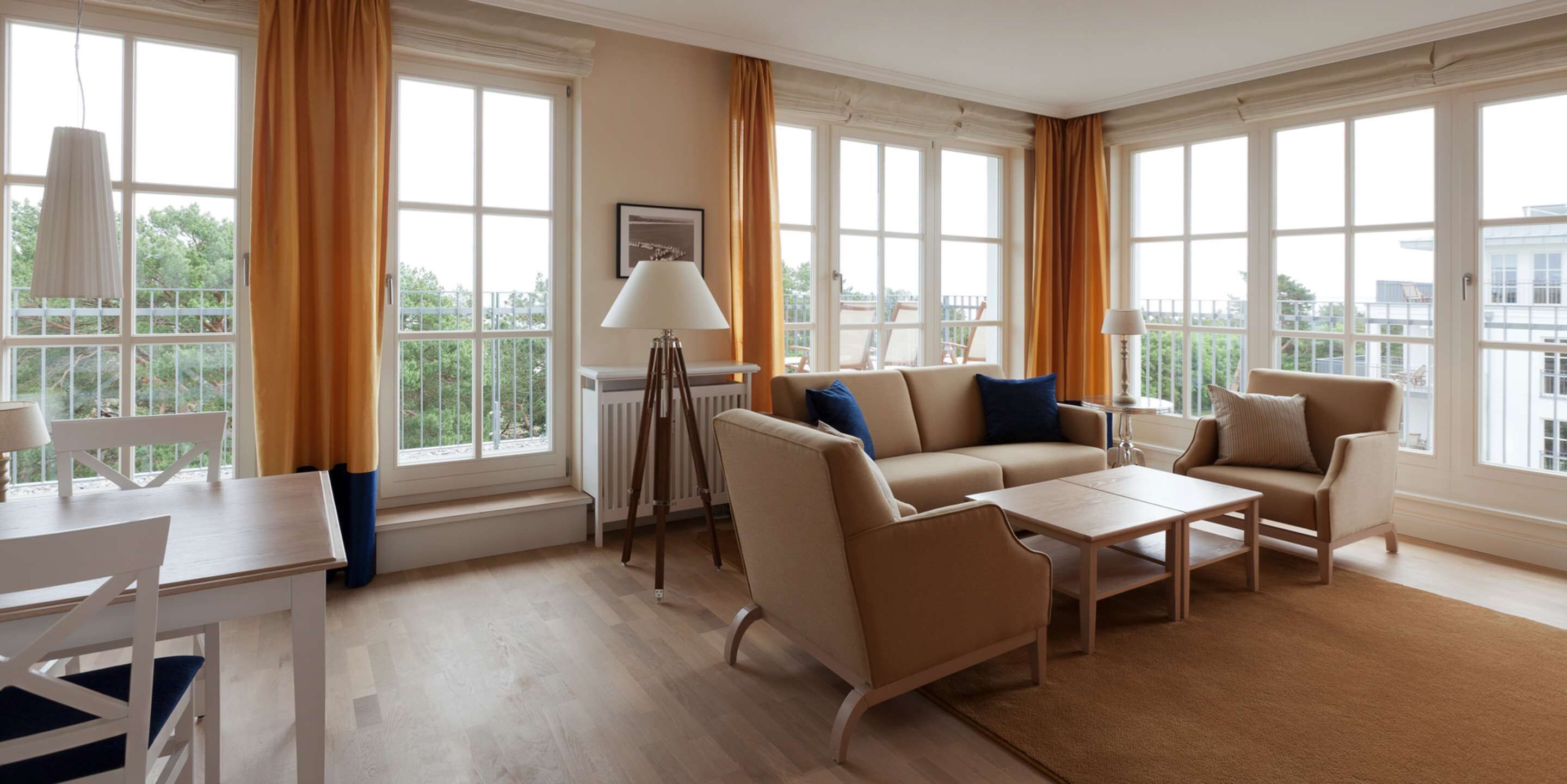 Uma sala de estar espaçosa com um conjunto de sofás, uma mesa de centro e um espaço de jantar com mesa e cadeiras. Grandes janelas proporcionam luz natural e vista para o exterior.