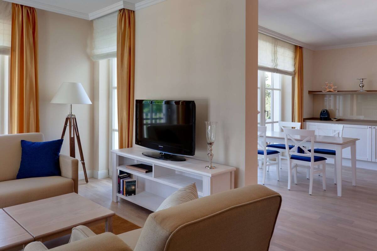 A modern living room with a sofa, coffee table, and TV. There is a dining area with a table and chairs.