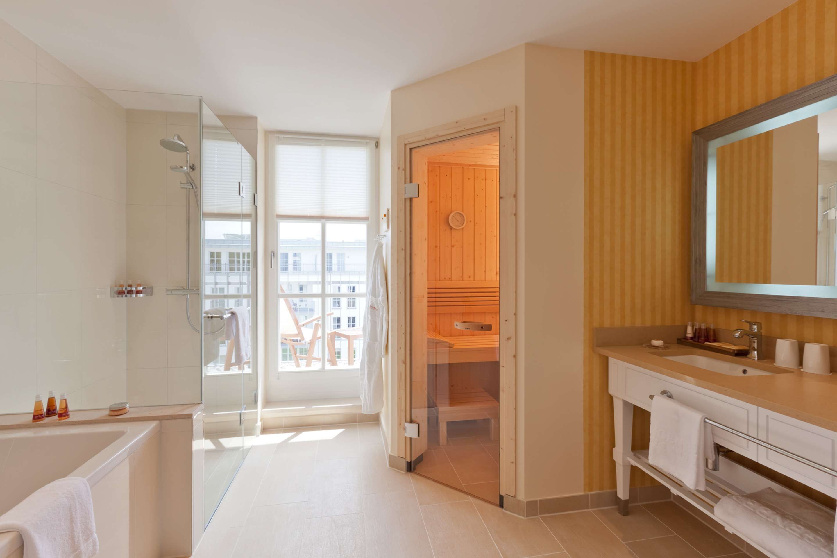 Een moderne badkamer met een douche met glazen wand, een houten sauna, een grote spiegel en een wastafel met bijpassend meubilair.