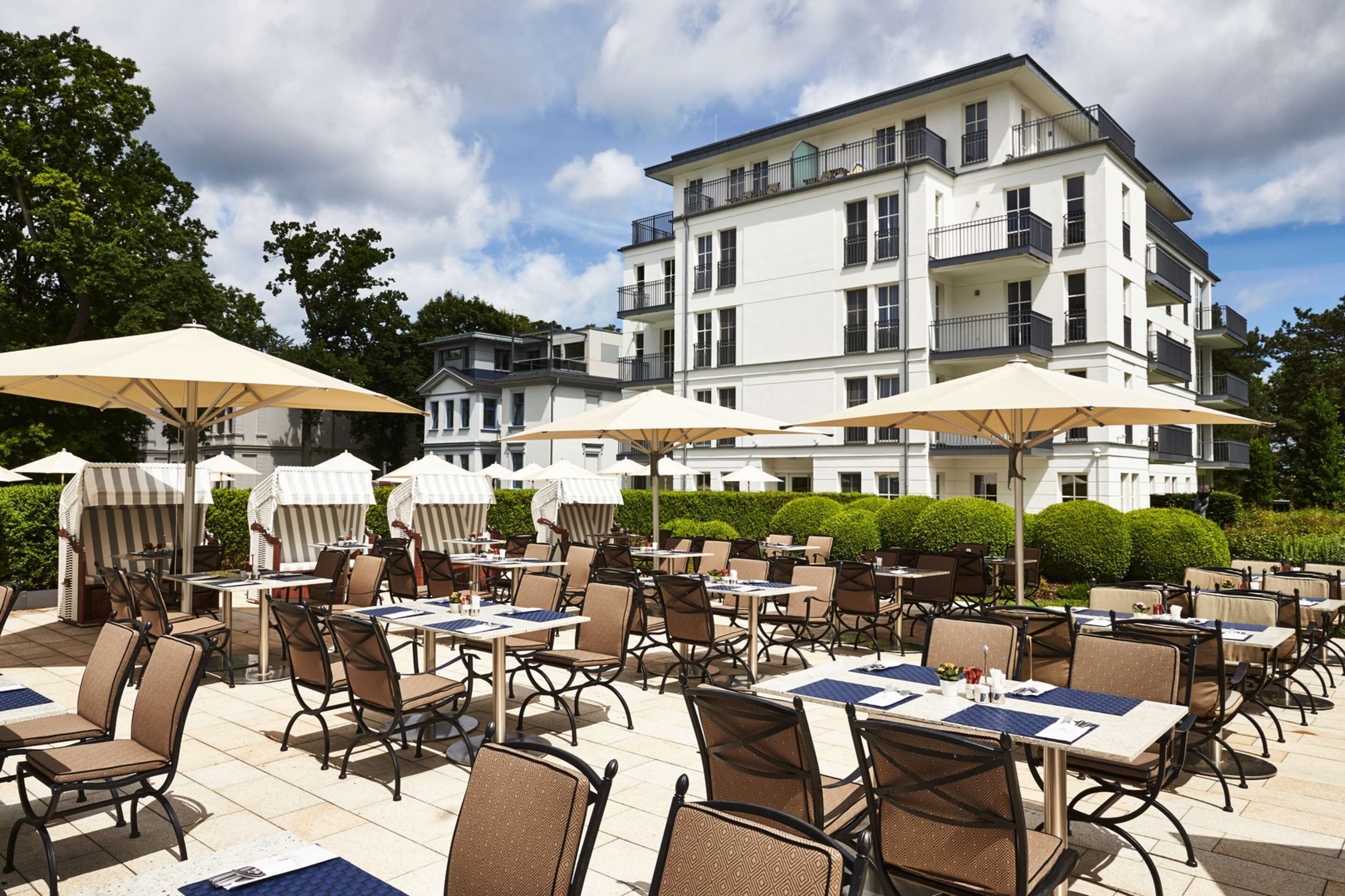 Un espace extérieur aménagé pour les repas, avec des tables, des chaises, des parasols et un bâtiment en arrière-plan.
