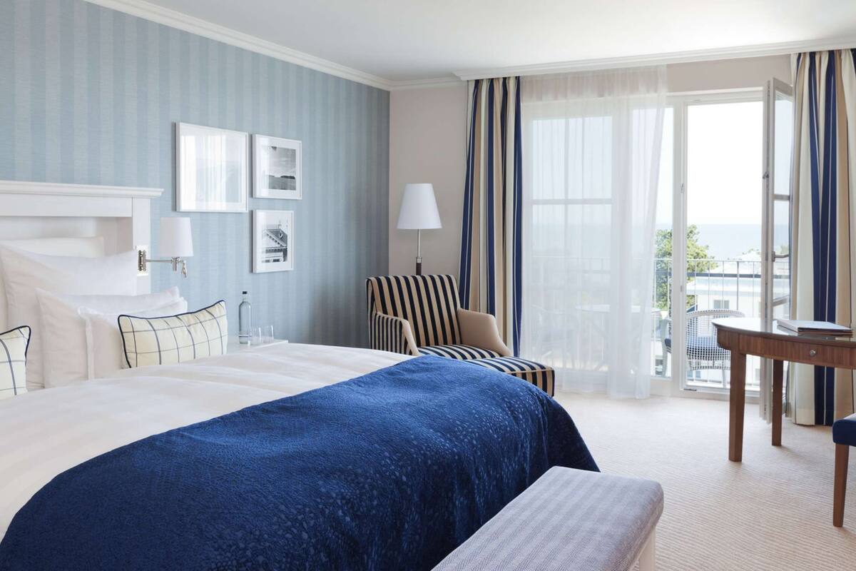 A hotel room with a large bed, a desk, a chair, and a view of the outdoors.