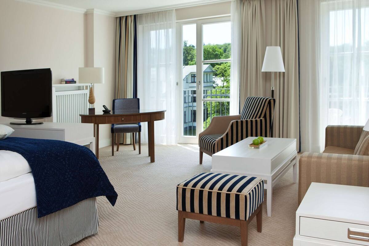 A hotel room with a bed, a desk, a chair, a sofa, and a TV.