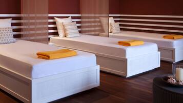A modern hotel room with two single beds, each with a white mattress and a yellow towel.