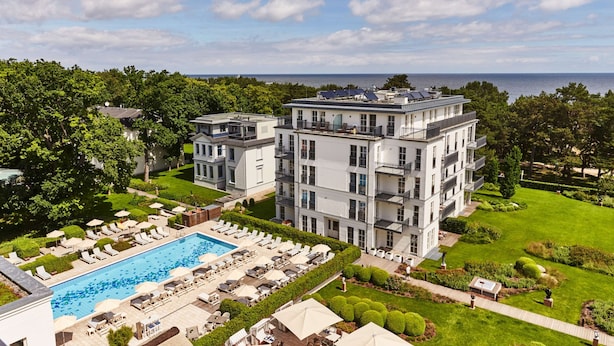 Un hotel moderno de varios pisos con piscina, tumbonas y un jardín bien cuidado.