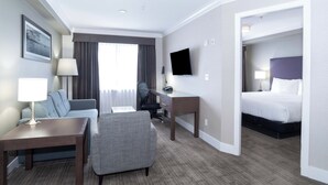 A hotel room with a bed, a desk, a chair, a sofa, a TV, and a window with curtains. - Sandman Hotel & Suites Abbotsford (Abbotsford)