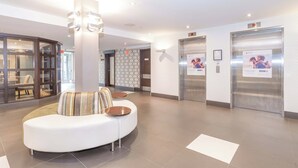 A modern lobby with a curved white sofa, two small wooden tables, and two elevators. - Sandman Hotel & Suites Abbotsford (Abbotsford)