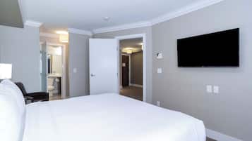 Habitación de hotel con una cama grande, un televisor de pantalla plana montado en la pared y una puerta que da a un baño y otra habitación.