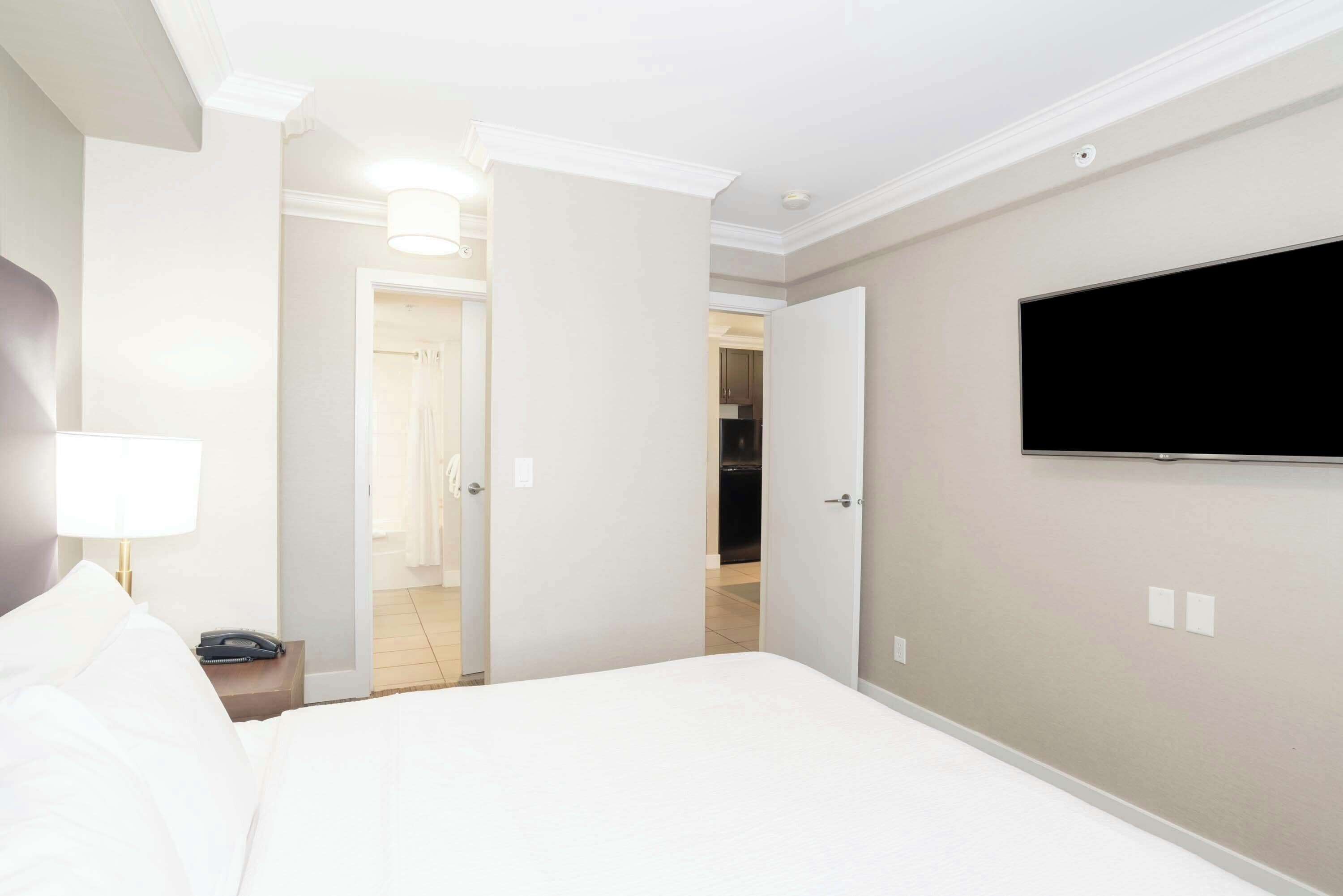 Habitación de hotel con cama, televisión montada en la pared, lámpara de noche y puerta que da a un baño.