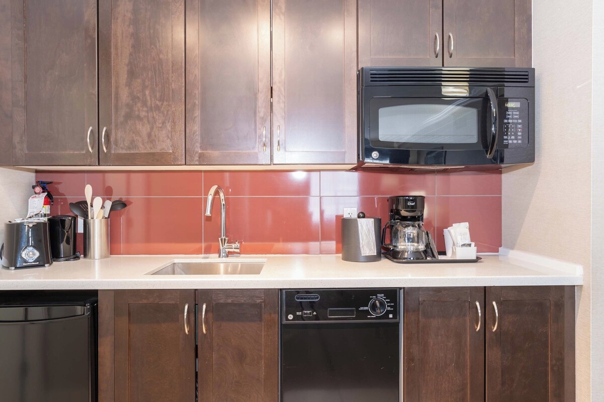 Una cocina con armarios de madera, microondas, lavavajillas y cafetera.