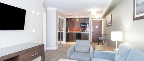 A modern living room with a flat-screen TV, a grey sofa, a coffee table, and a dining area with a table and chairs.
