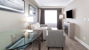 A hotel room with a glass table, a sofa, a TV, and a fireplace. - Sandman Hotel & Suites Abbotsford (Abbotsford)