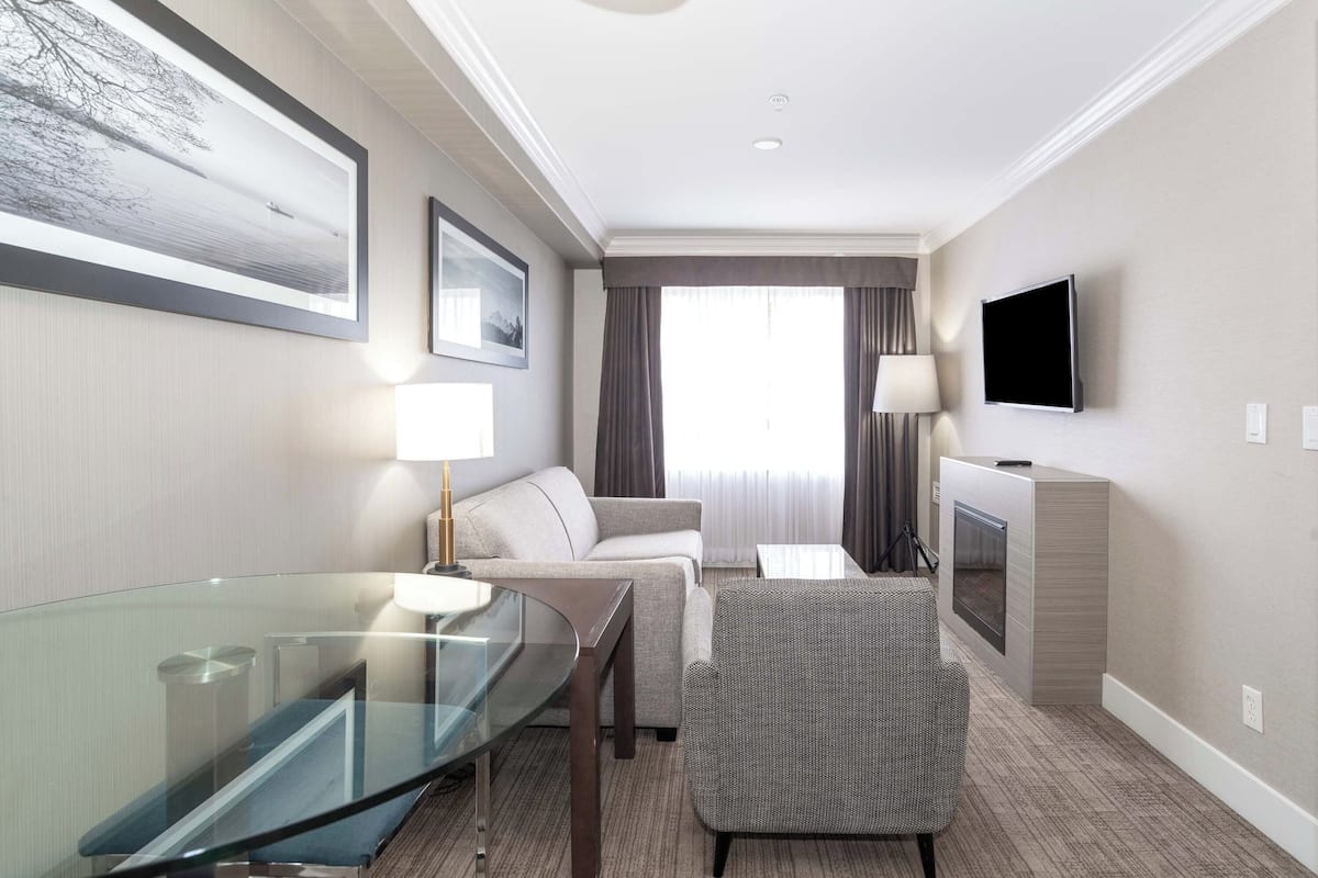 A hotel room with a glass table, a sofa, a TV, and a fireplace.