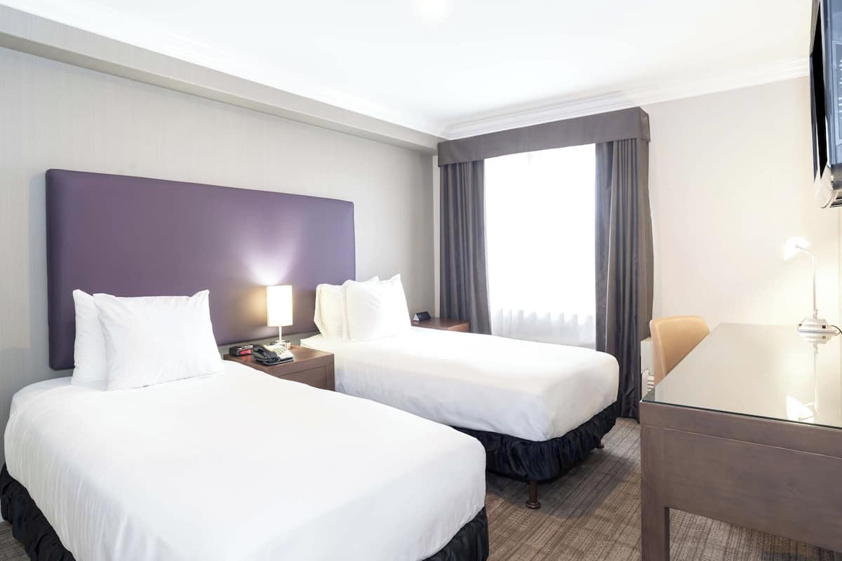 Ein Hotelzimmer mit zwei Betten, einem Schreibtisch und einem großen Fenster mit Vorhängen.